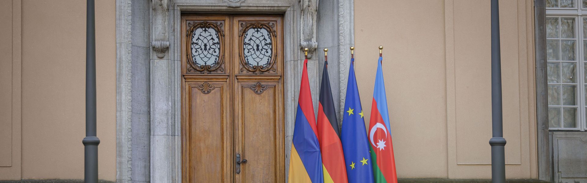 Trilateral meeting at Villa Borsig in Berlin between Germany, Armenia, and Azerbaijan, with their flags displayed alongside the European Union flag at the entrance.